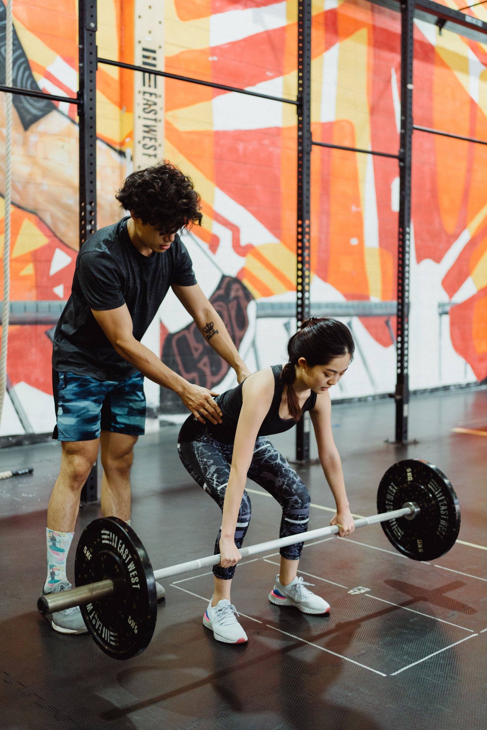 A coach guiding a client through a barbell lift.